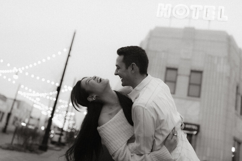 A couple laughing and dancing together under string lights outside a vintage hotel in downtown Indianapolis.