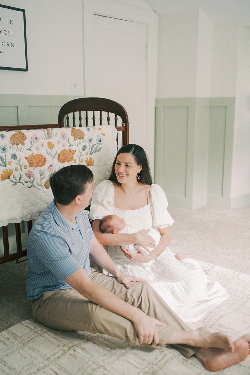 mom and dad sitting in nursery holding baby smiling at each other