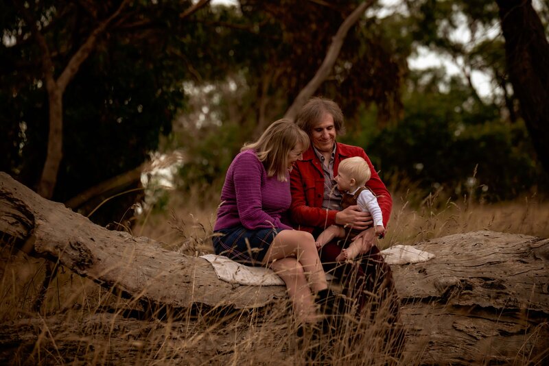 parents seated on log with 9 month old son