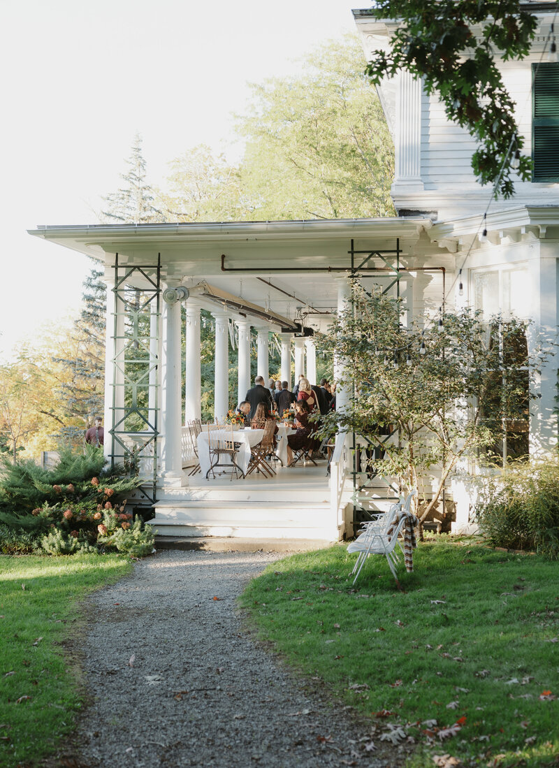 A candid photo of the cocktail hour at the wadsworth homestead in geneseo, NY. The sun illuminating the back porch as guests enjoy live music and cocktails. Photo by Dash and Boheme Photography. 