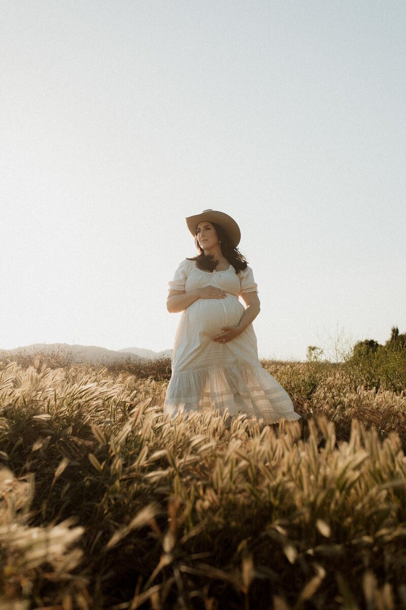 Expectant mother standing in a wide open field at golden hour in Menifee, CA.