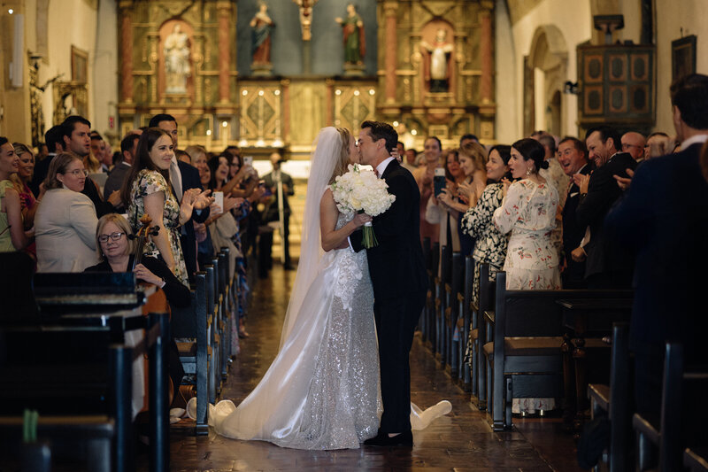 Bride and groom sharing a kiss during the wedding ceremony recessional, captured in a candid, photojournalistic style, showcasing an authentic and emotional moment.