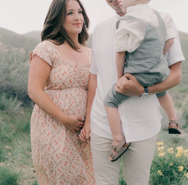 Mountain maternity session featuring an expecting mother in flowing dress with serene lake views. PHOTOGRAPHED BY Salt Lake City newborn photographer