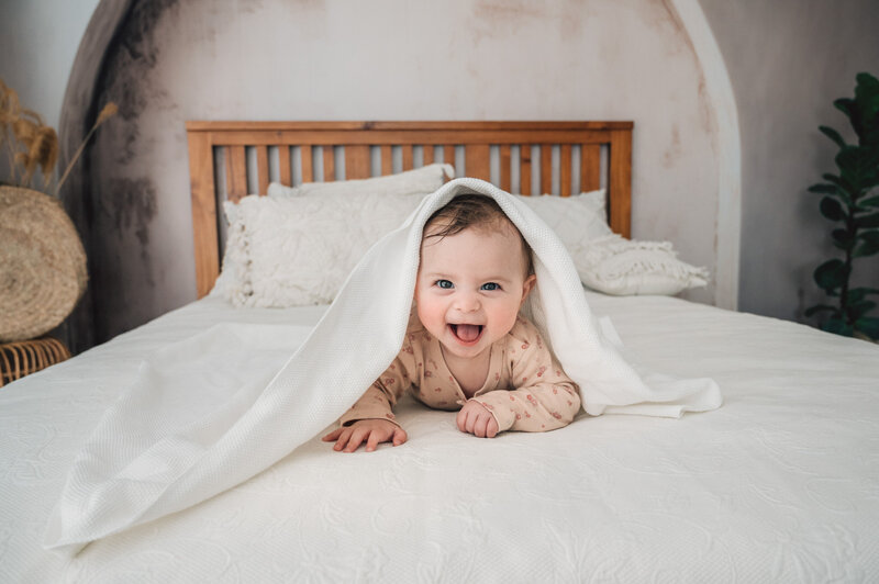 baby girl smiling, hiding in a blanket