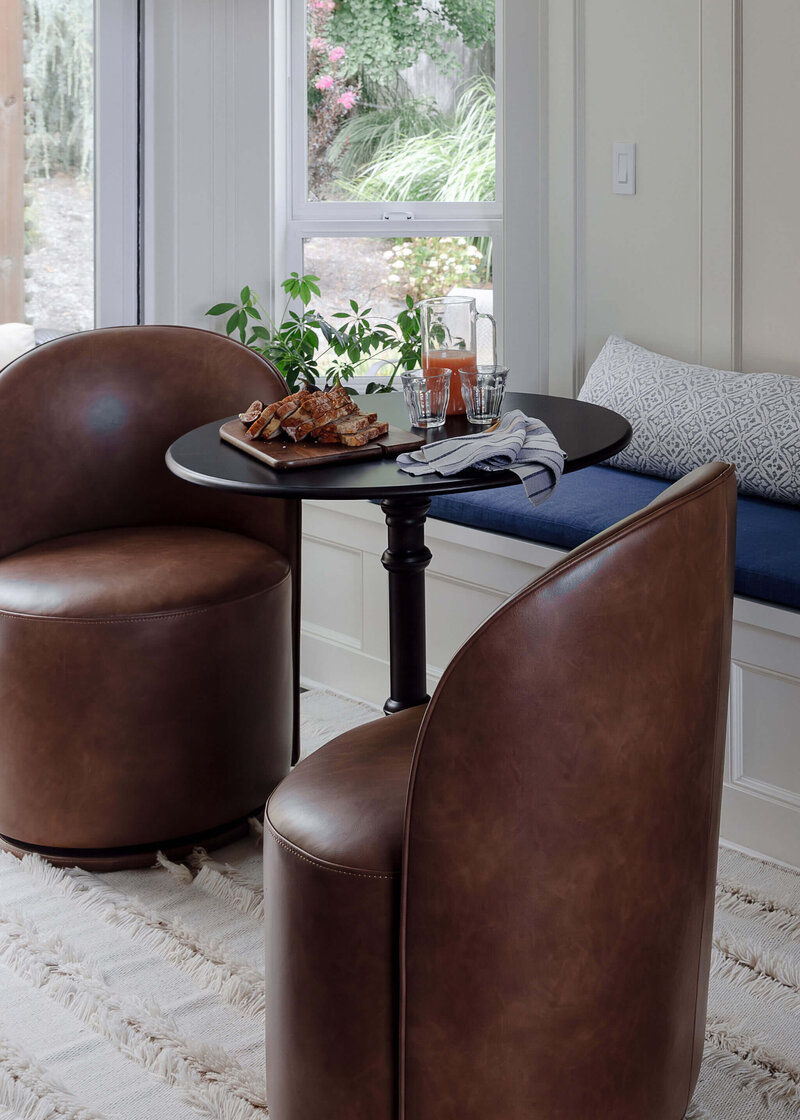 A seating corner with brown leather chairs, a black table set with food and drinks and a built in wall bench.