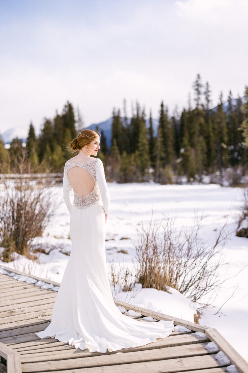 Capture the breathtaking beauty of a bride standing by herself on her wedding day in Canmore, with a frozen stream as the perfect winter backdrop. A serene and elegant moment in the heart of the Canadian Rockies.