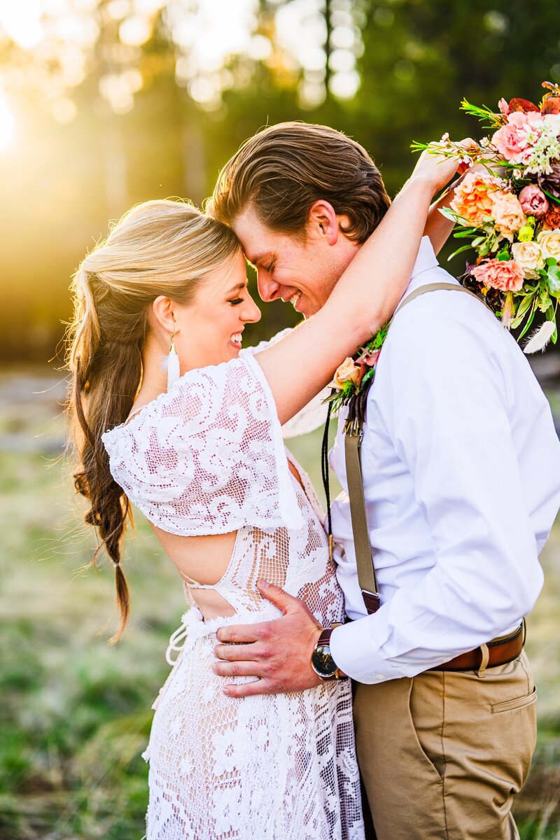 bride and groom touching foreheads together smiling with golden hour sunset behind them and pine trees at Arizona Nordic Center wedding elopement