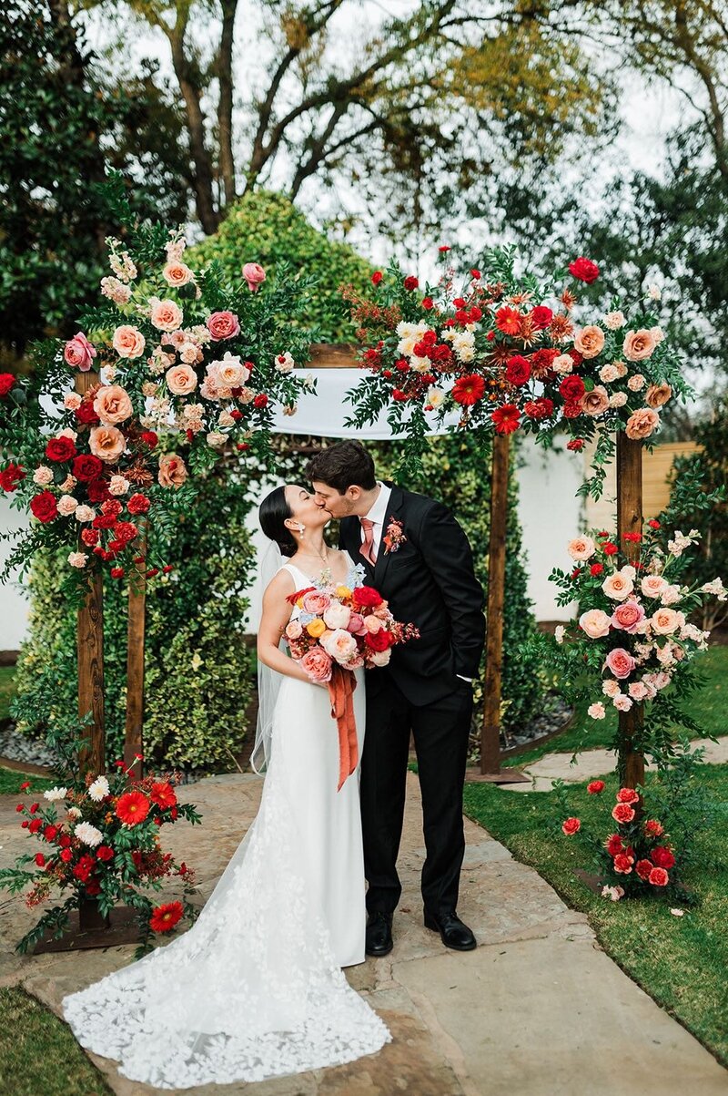 Bride and groom kissing under flower arch at wedding planned by Bianca Nichole and Co