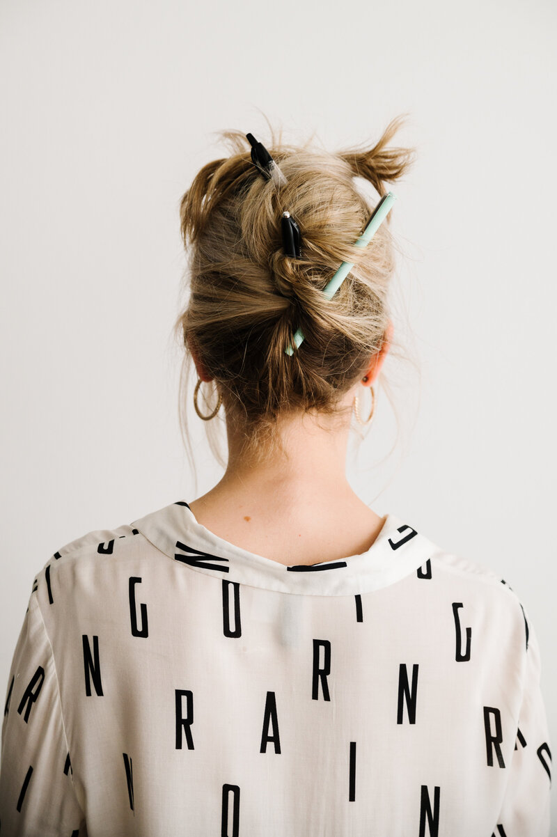 The back of Sarah Klongerbo wearing a white shirt with black letters on it and her hair held up with pens