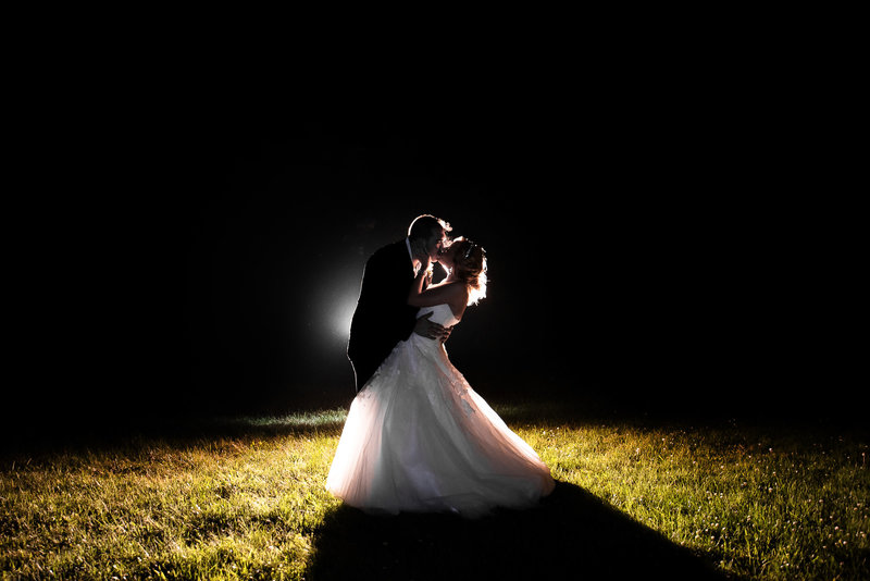 Backlit photo of a groom dipping and kissing his bride