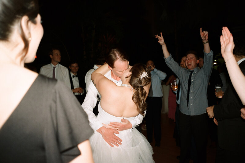 Film photo of a couple kissing in the middle of a cheering dance floor during their winter wedding at Roger Williams Botanical Gardens in Rhode Island — photographed by a film wedding photographer.