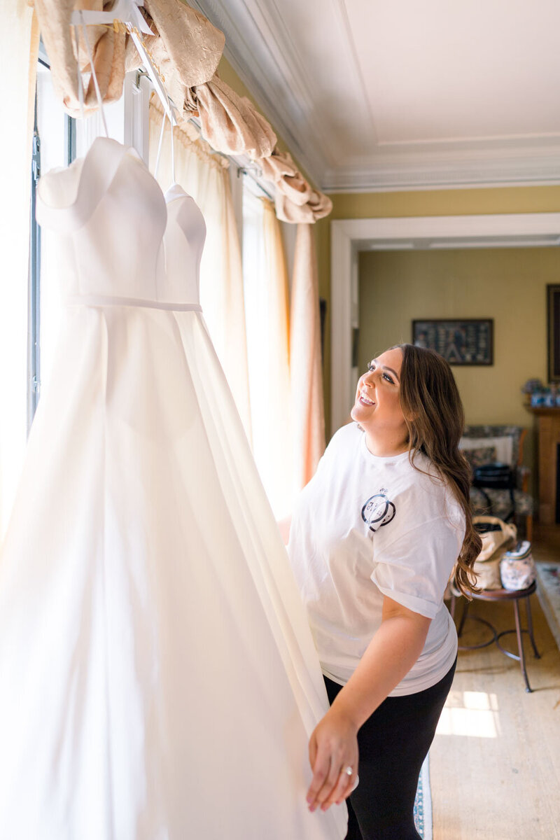 A bride admiring her wedding gown hanging by the window