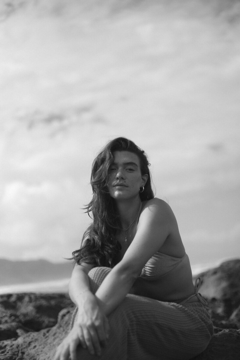 Black and white photo of girl sitting on rocks on the beach