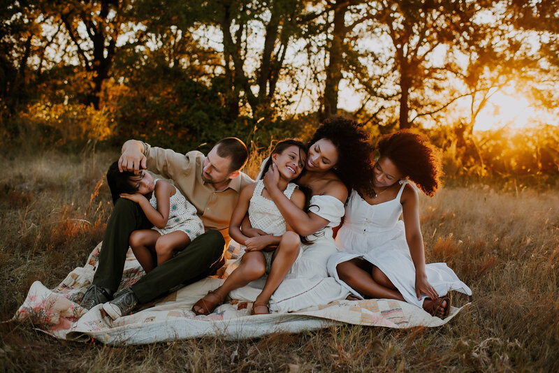 A beautiful mixed race family sitting on a picnic blanket by Grapevine Lake in Flower Mound, TX at sunset