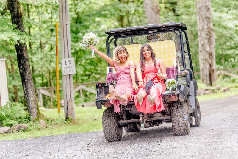 Two bridesmaids cheer while riding on the back of a Gator 4 x 4