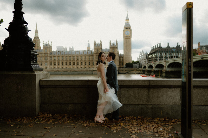 bride and groom standing, bodies close facing each other, as the groom looks at his bride and the bride looks over her shoulder toward the camera, with westmister behind them
