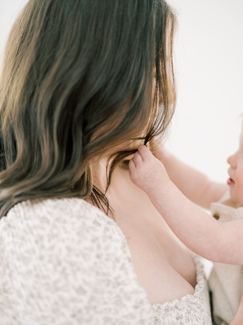 One year old twin son plays with brunette mother's hair at Little Rock studio taken by photographer Little Rock Bailey Feeler