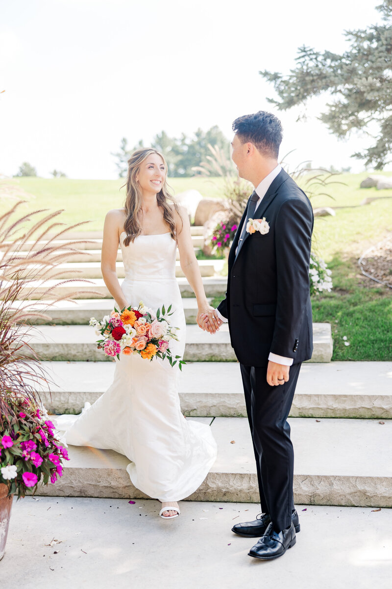 a groom smiling at his bride while helping her down the stairs