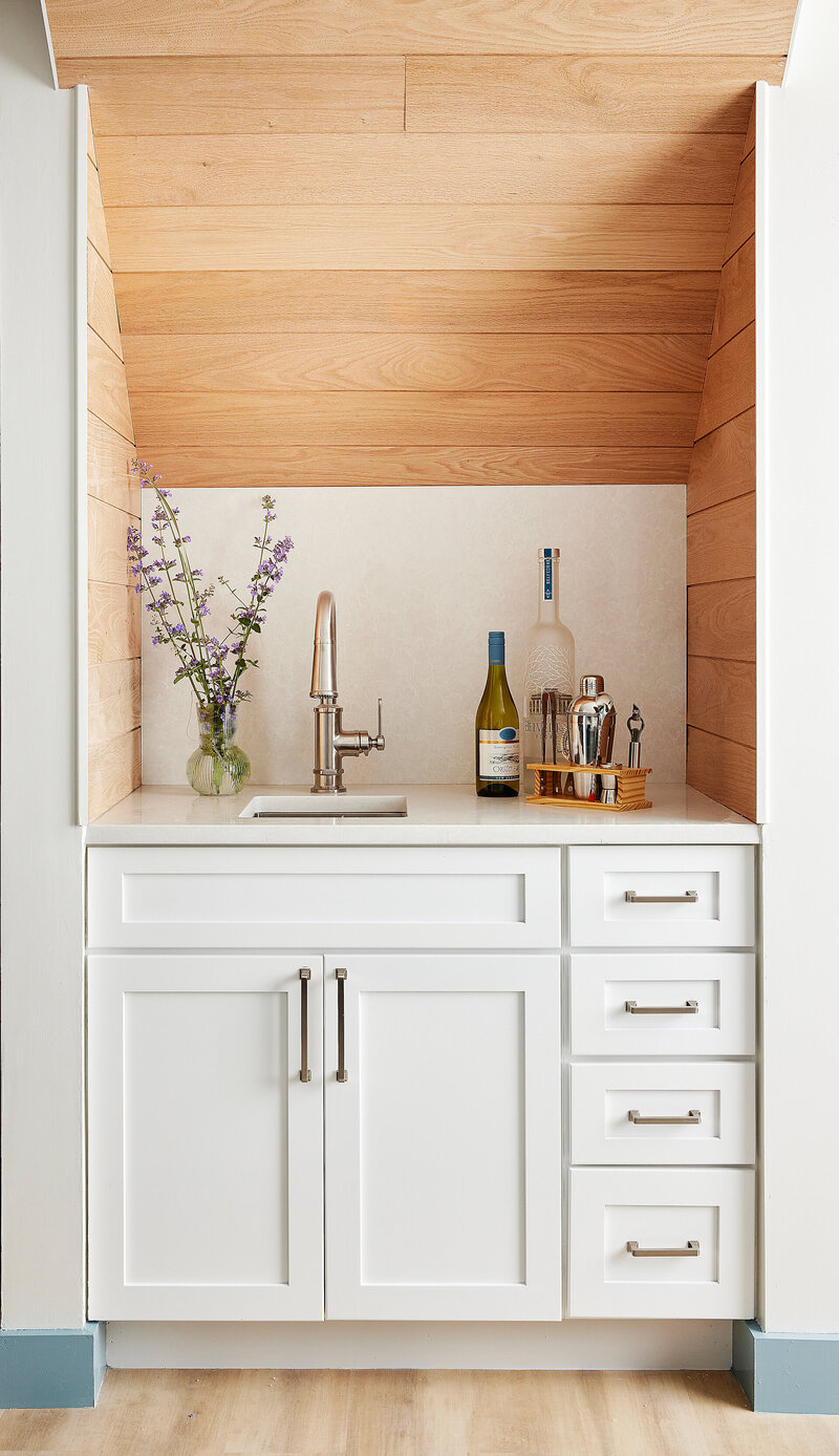 Modern kitchen featuring white cabinets, wooden shelves with decorative items, and a vase with flowers, creating a stylish and functional space