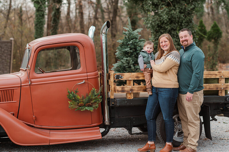Family of three standing next to vintage red truck with Christmas trees in York, PA
