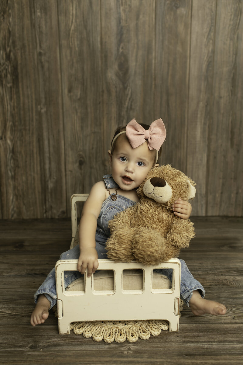 One-year-old baby girl playfully sitting on a bed