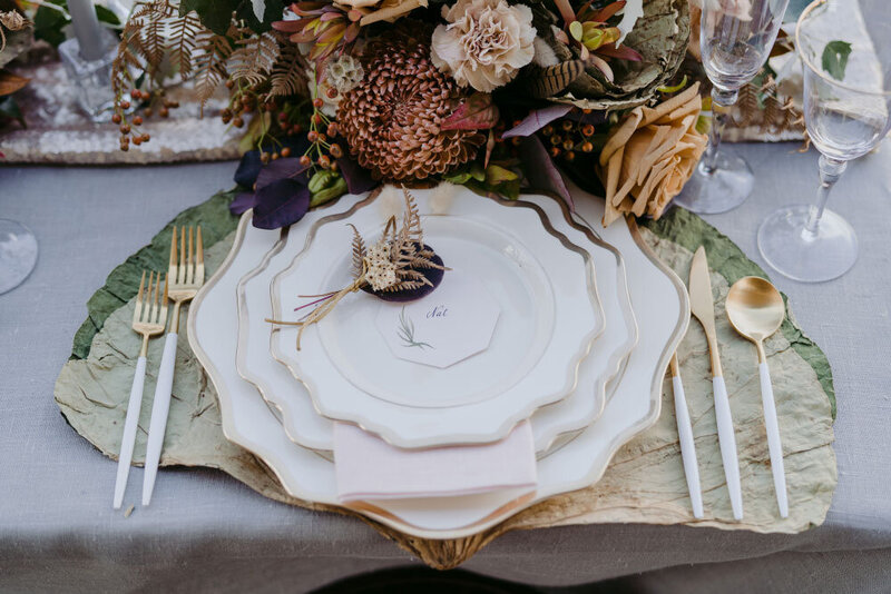 Octagon place card at wedding reception with white and gold plates and cutlery.  Dried flowers with mustard and gold and purple colours decorate the wedding reception table