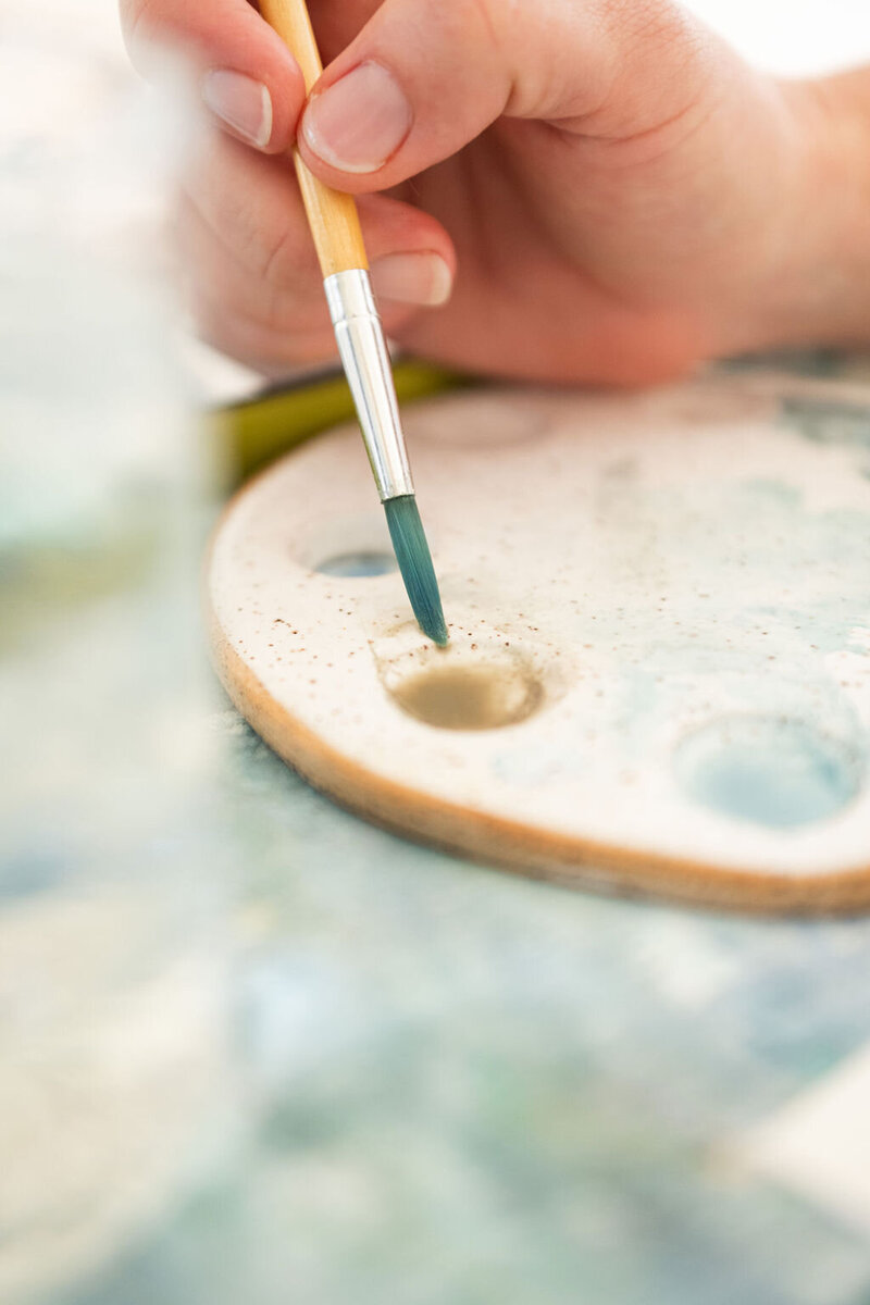 an artisti's hand dipping a paintbrush into water preparing to paint