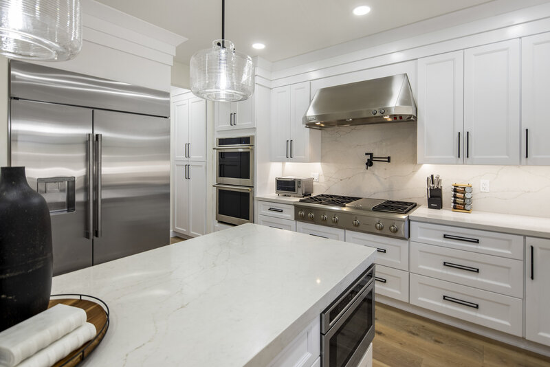 white countertops. white cabinets with gold harware. stainless steel refrigerator. large island.
