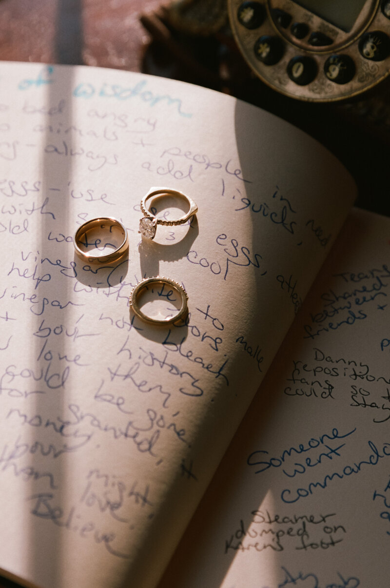 Film photo of three gold wedding rings placed on handwritten vows in soft natural light — a poetic wedding detail made by a film wedding photographer.