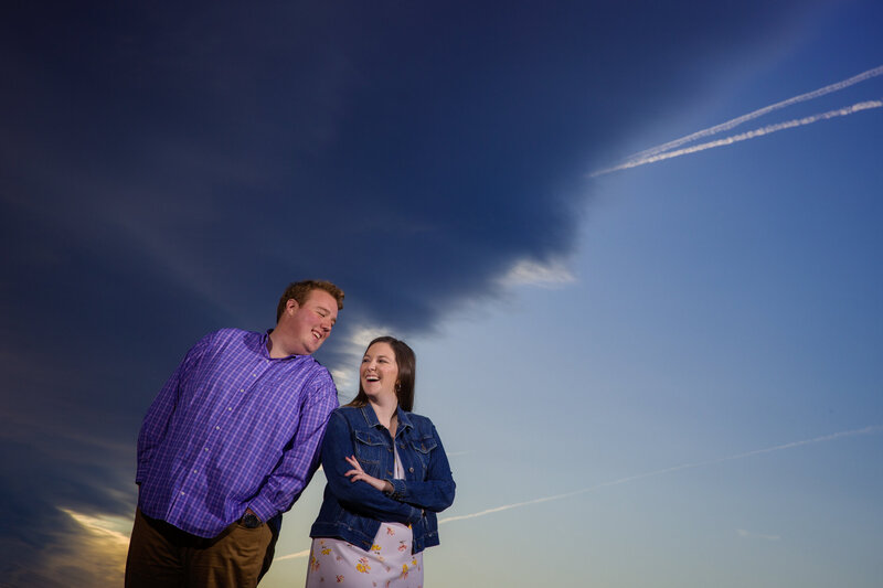 Couple standing together with dramatic clouds in the background, creating a unique and striking engagement photo.