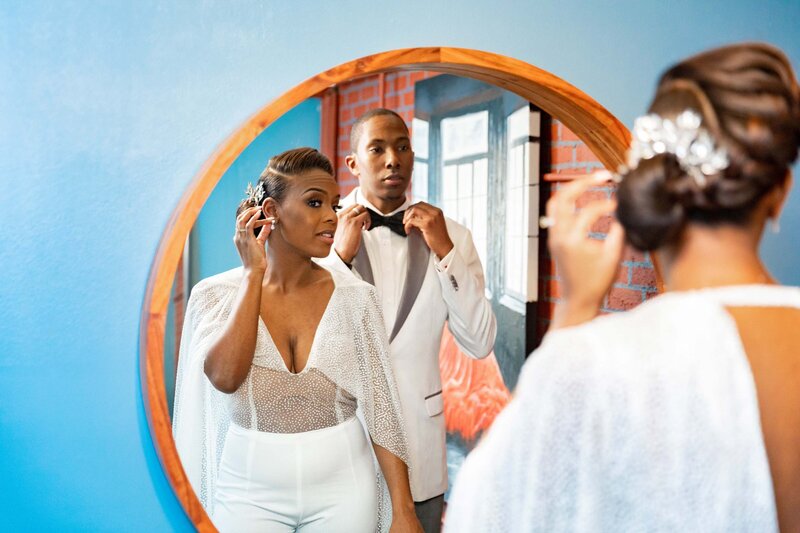 A bride adjusting her earrings while her groom adjusts his bow tie.
