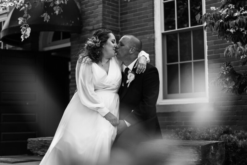 Bride and groom kissing on a bench outside the Schoolhouse in Fairview PA