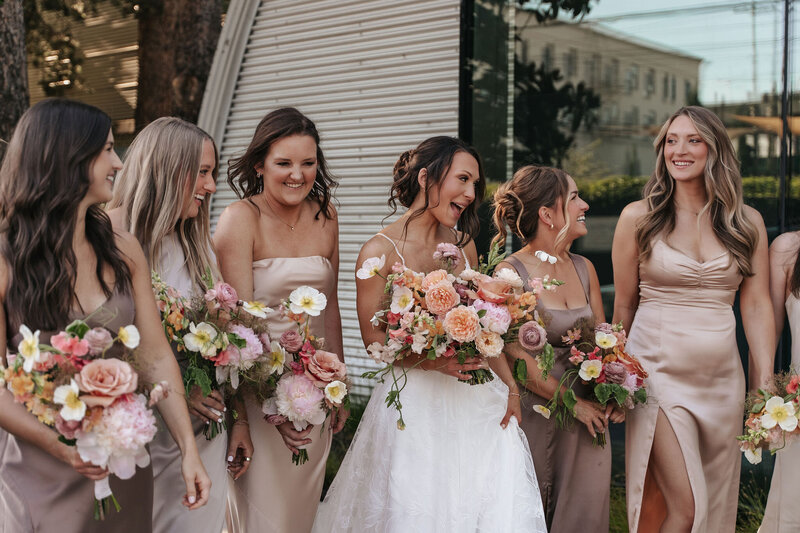 Candid moment where a wedding party is walking together at Blockhouse Venue near Downtown Portland, wearing long dresses and holding pink and blush floral bouquets, perfect for elegant urban wedding celebrations.