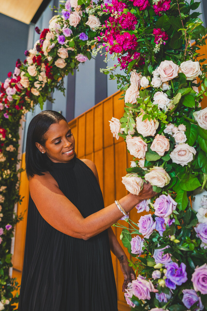 Marcia Alphonso weddings and events floral designer arranging a lush ceremony arch installation featuring greenery and pastel roses in a vibrant, elegant design.