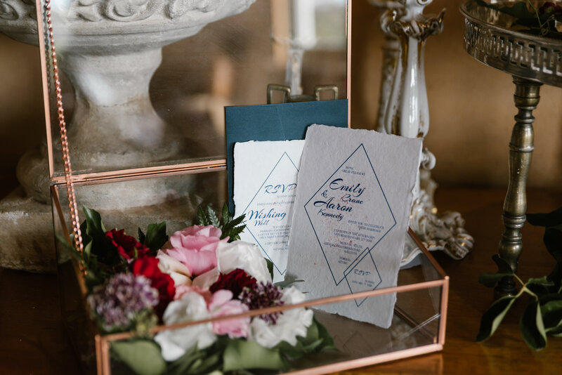 White wedding invitations with soft deckled edge and blue diamond design, in vintage glass case with flowers