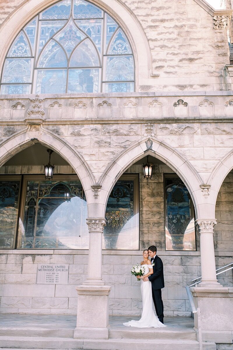 A bride and groom pose in front of a historical United Methodist church in Asheville NC