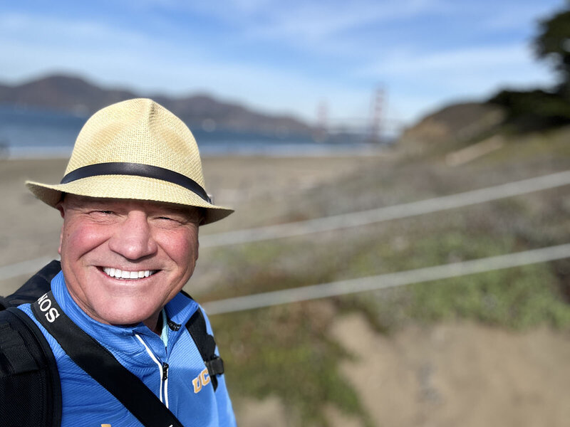 Close up of a smiling man on a beach wearing a Fedora 