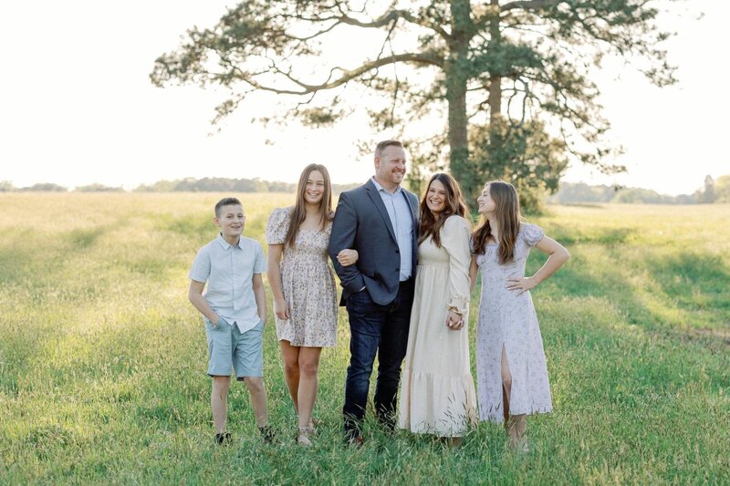 A family of five standing in a sunlit field, smiling and posing for a Virginia Wedding Photographers photo.