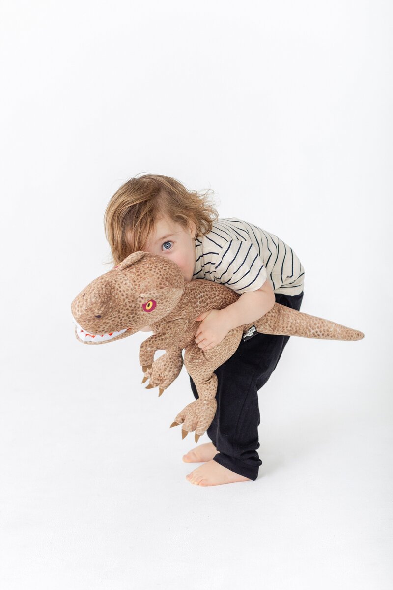 humorous studio portrait of toddler holding t-rex stuffed animal