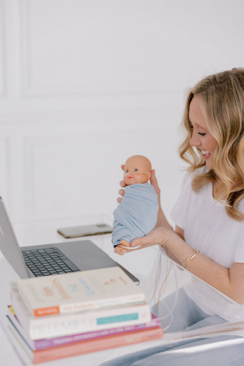 woman holding a baby smiling at a laptop