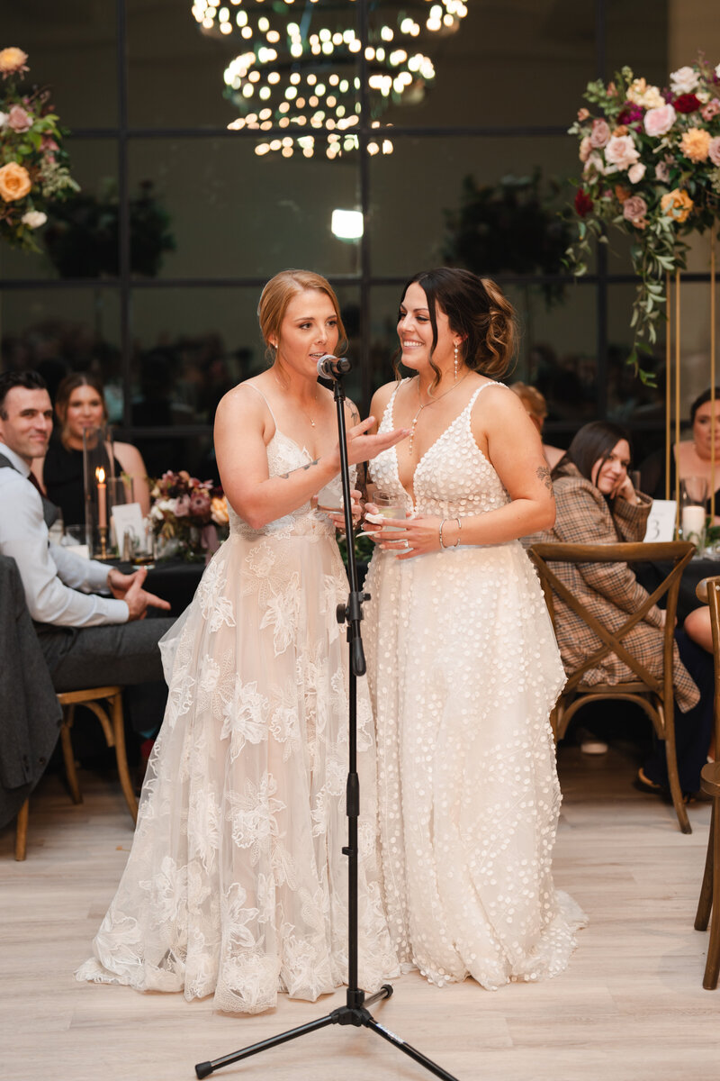 the brides give a speech at their wedding reception in honor of each other