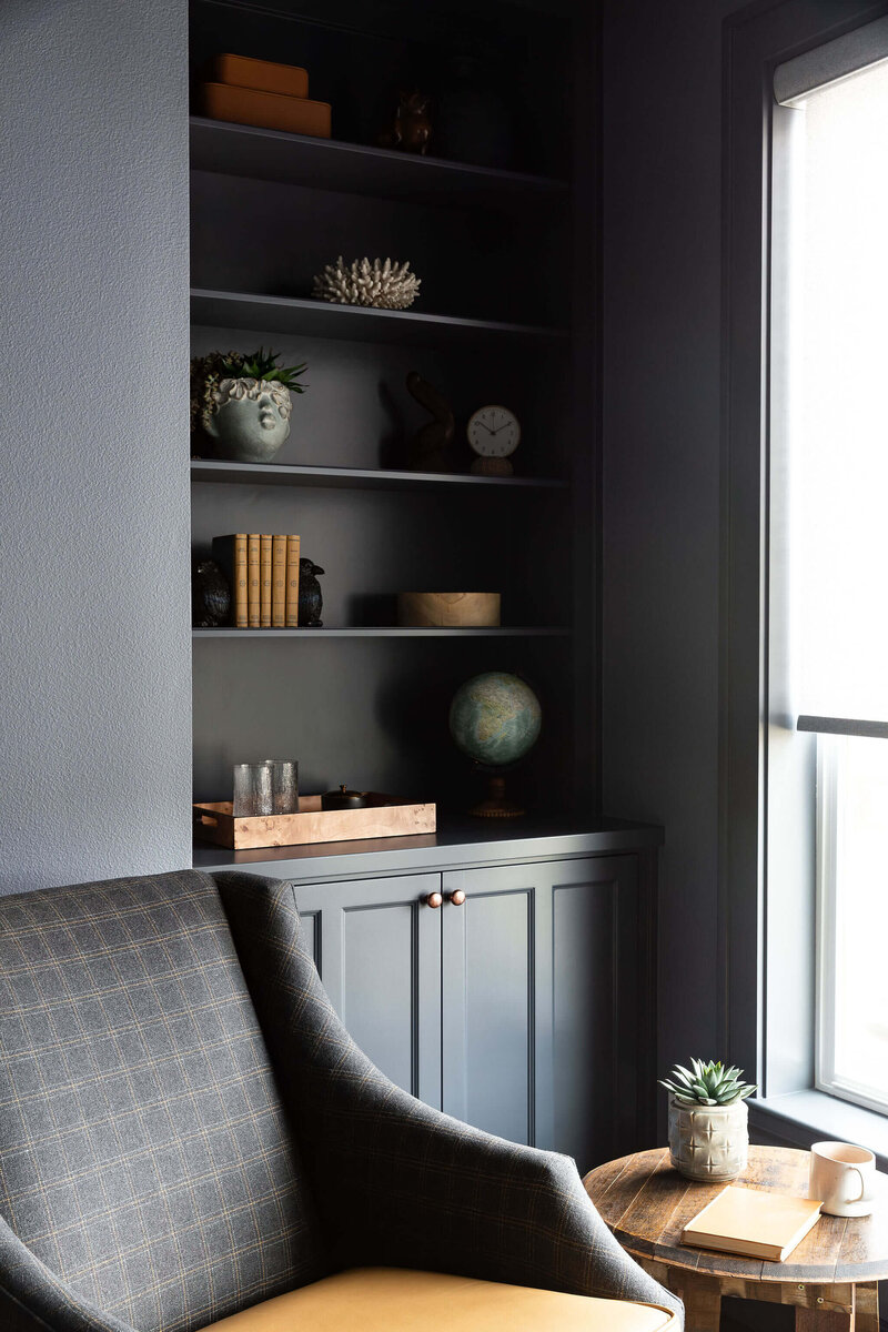 A cozy study corner featuring a built in bookcase, wool and leather upholstered chair, and a wooden side table.
