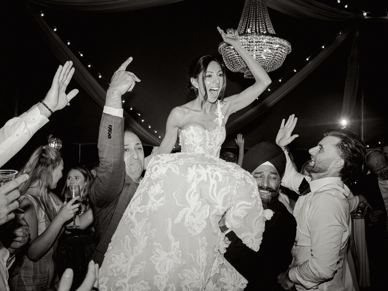 Black and white photo of bride getting lifted up on guests shoulders during wedding open dancing