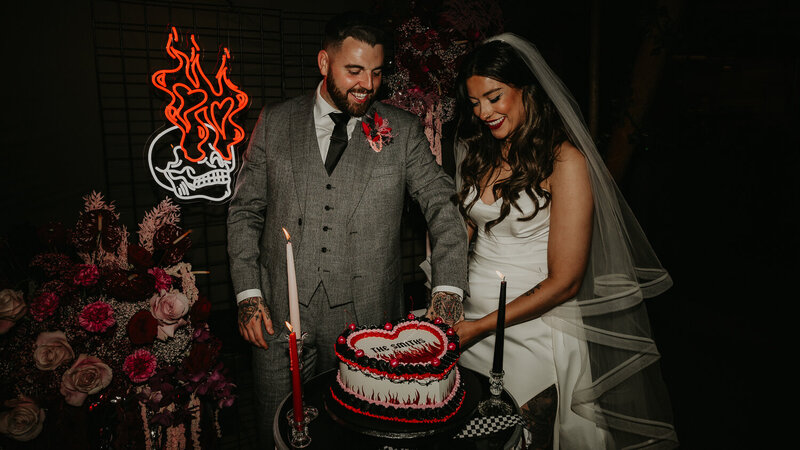 A wedding couple blow pink and red confetti at the camera.