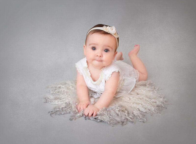 Baby girl at 6 months old taking pictures at studio wearing a white outfit nd smiling