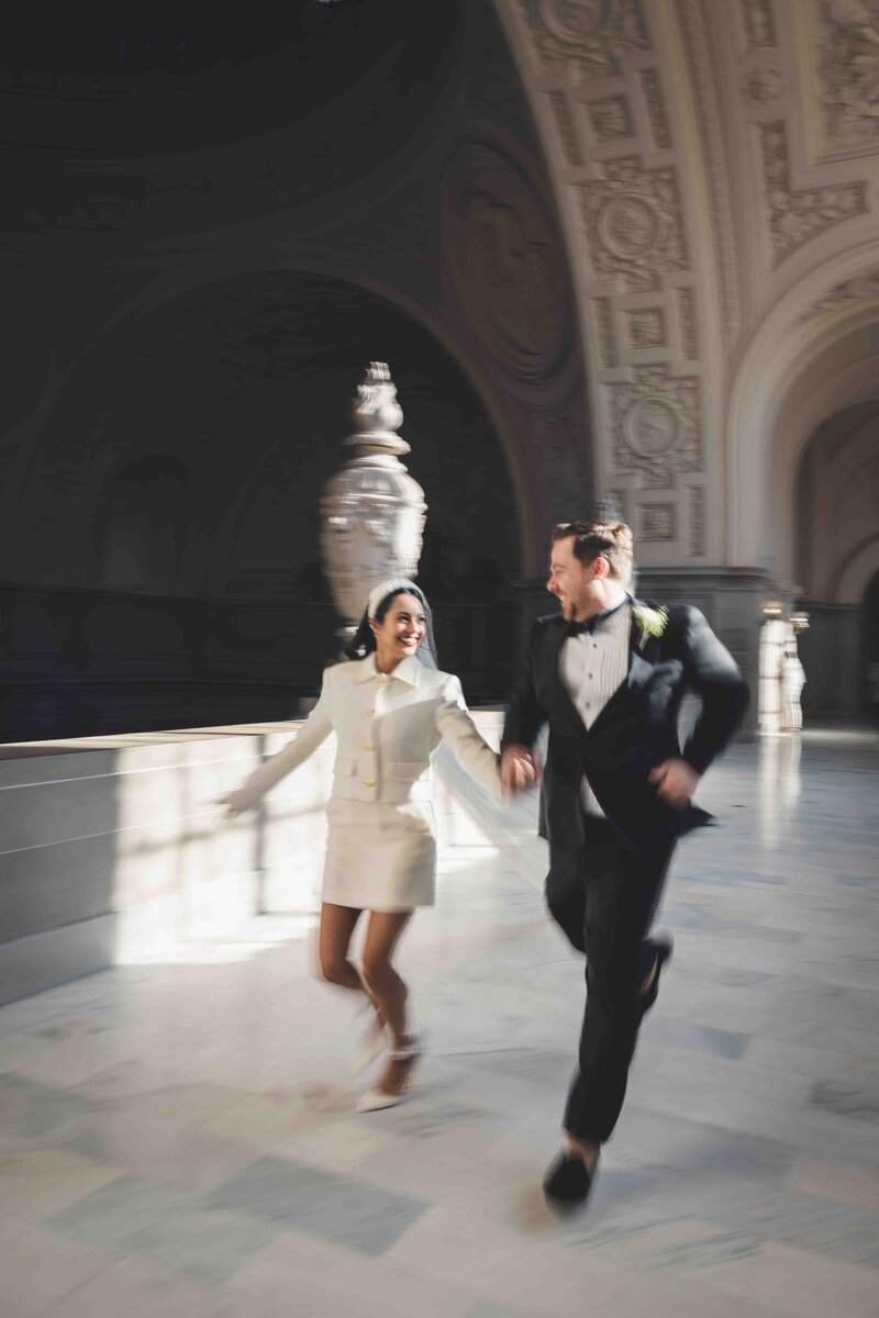 A motion blurred portrait of a bride and groom running across the terrace of a courthouse with an engraved marble flooring and dome