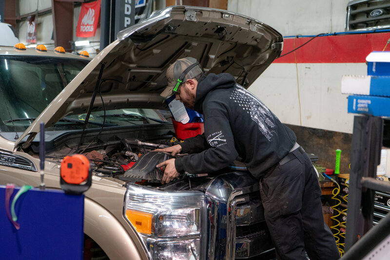 A mechanic repairs a Ford and replaces an air box