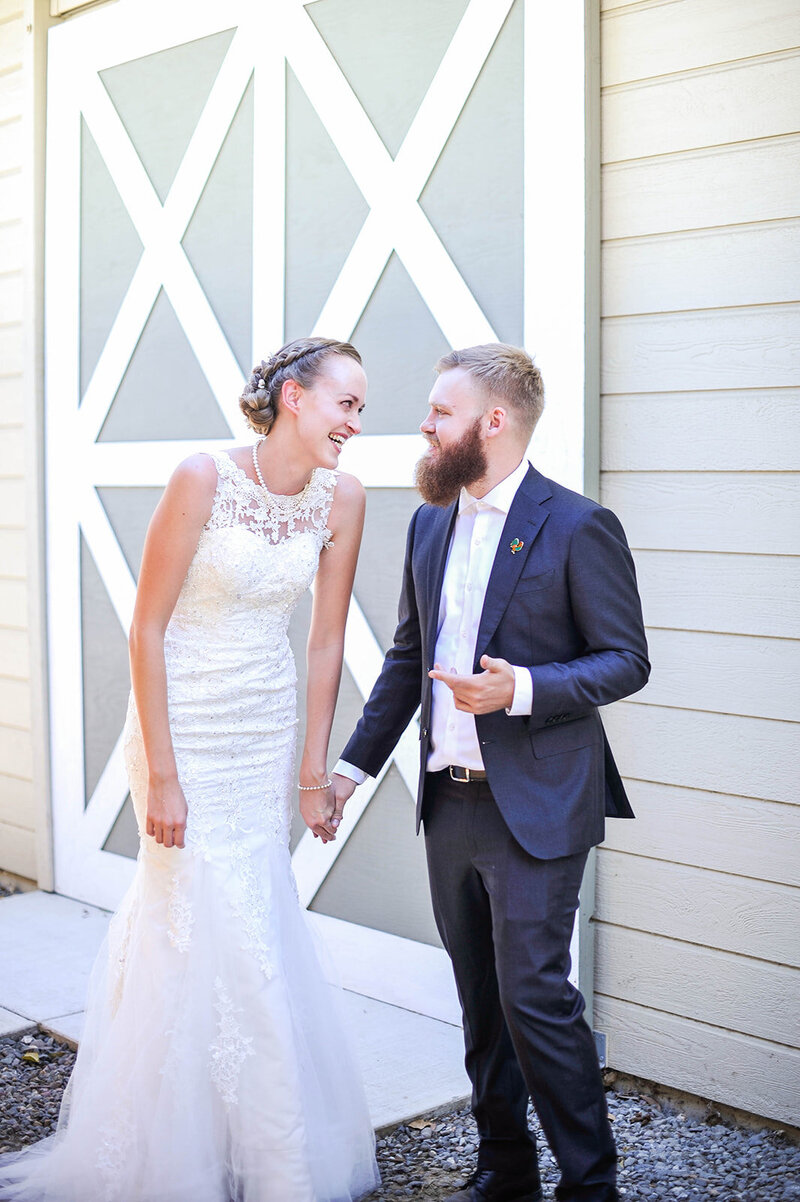 Bride in fitted laced detailed wedding dress with mermaid tail holds hands and laughs with groom in blue suit