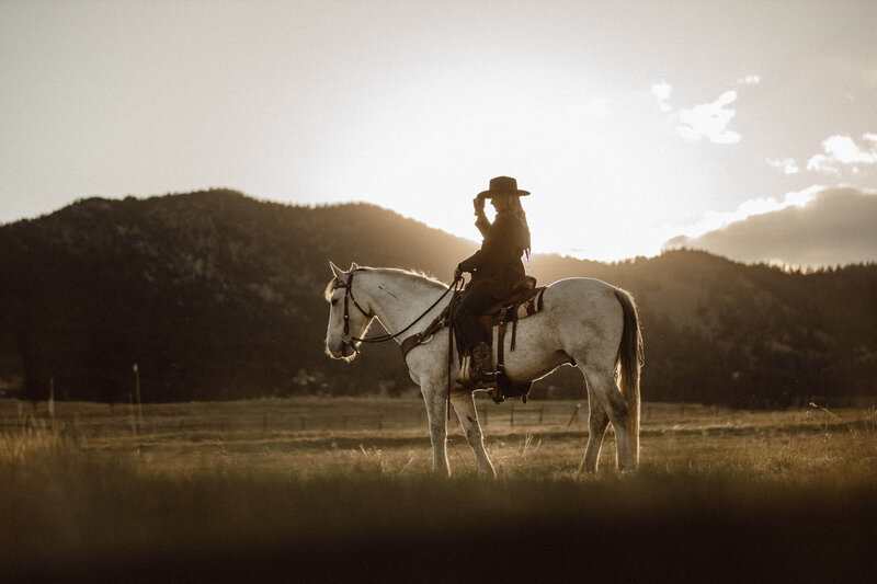 cowgirl touching her hat on a horse at sunset
