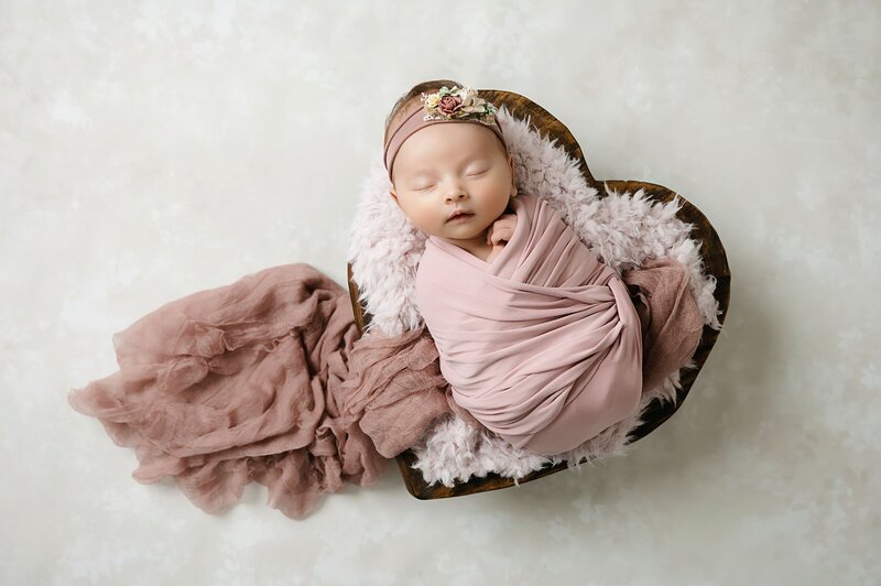 baby girl wrapped in yellow sleeping in tiny bed on backdrop with gold stars